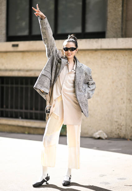 Model Xiao Wen Ju is seen wearing a gray blazer, tan shirt, cream pants and black shoes with black sunglasses outside the Miu Miu show during...