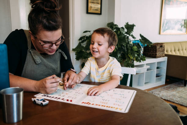 mom painting smiling son's finger nails at kitchen table - nails art photos et images de collection