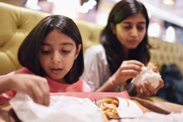 mother and daughter (6-7 years) eating burger and fries - junk food stock pictures, royalty-free photos & images