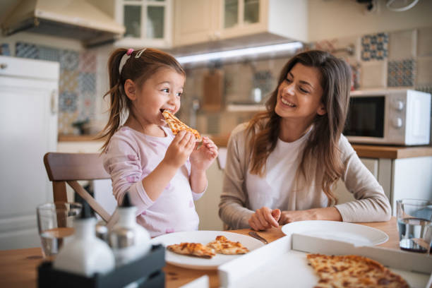 mother and daughter eating pizza at home. - junk food stock pictures, royalty-free photos & images