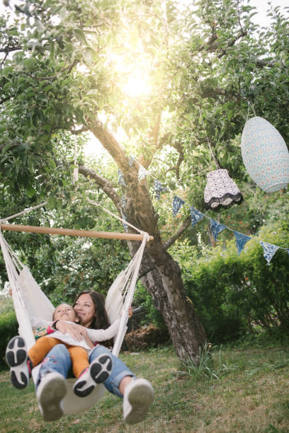 mother and daughter smiling while swinging on hammock in backyard - garden decoration stock pictures, royalty-free photos & images