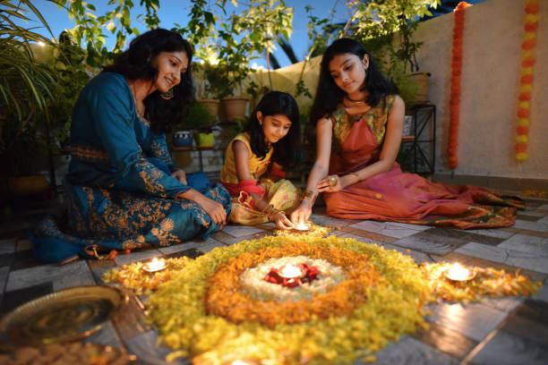 mother and daughters lighting lamps around rangoli made using petals - home decoration stock pictures, royalty-free photos & images