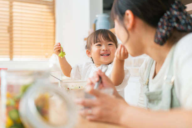 mother and her small daughter enjoying eating salad and drinking smoothie at home - food stock pictures, royalty-free photos & images