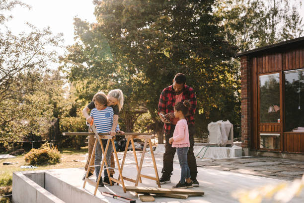 mother and son using hand saw while father talking to daughter outside house - garden decoration photos et images de collection