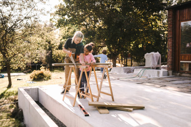 mother cutting wood with hand saw by daughter outside house - home decoration stockfoto's en -beelden