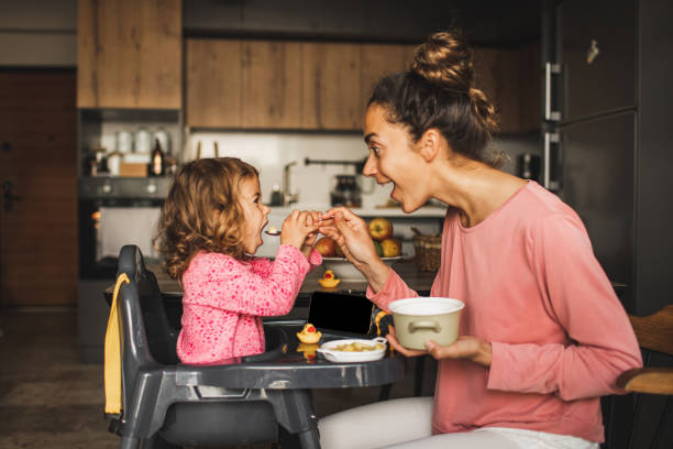 mother feeding little baby daughter and both having fun and laughing. harmony in family - food stock pictures, royalty-free photos & images