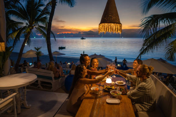 multiracial friends at the dinner at the beach restaurant toasting with wine - travel stock pictures, royalty-free photos & images