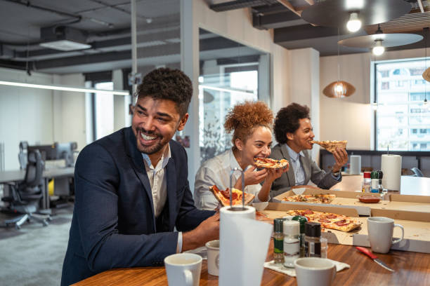 multiracial group of business people, eating a pizza for their lunch break at cafeteria - junk food stock pictures, royalty-free photos & images