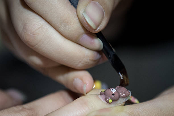 Nail artist Suzuki Ai paints a teddy bear design on a woman's fingernail at Ita Color's Yellow nail salon on February 27, 2014 in Akihabara district,...