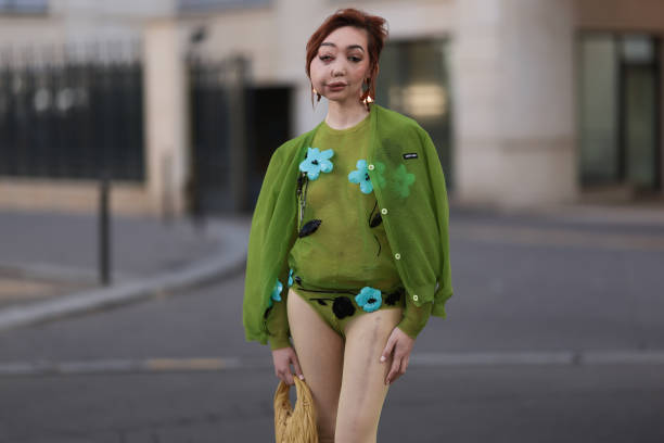 Nikki Lilly Christou is seen wearing a transparent green top with blue and black embroidered flowers, a green cardigan, a beige leather Hobo handbag...