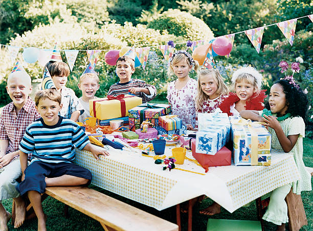 nine children sitting at a table at a birthday party - garden decoration stockfoto's en -beelden