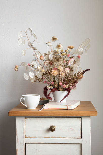 note pad, mug and arrangement of dried flowers on small cabinet - home decoration stock pictures, royalty-free photos & images
