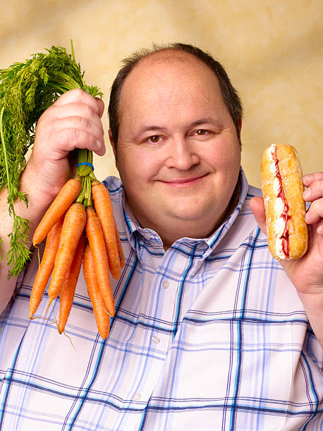 obese man with cream cake and carrots. - junk food stockfoto's en -beelden