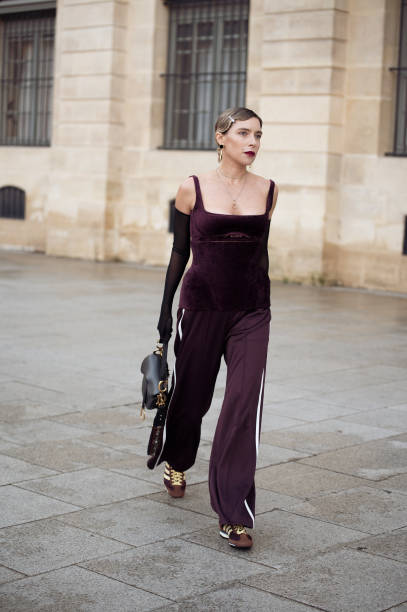 Olga Naumova wears burgundy pants with white stripe, brown adidas sneakers, burgundy corset top, black sheer long gloves, gold earrings and Dior bag...