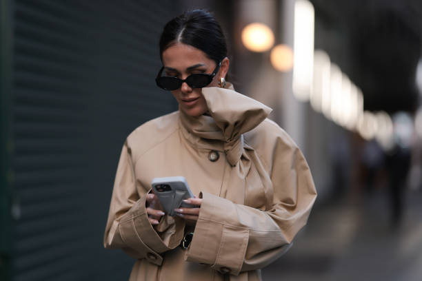 Olga Sokolenko seen wearing black sunglasses, gold / silver hoop earrings, 1811 Eighteen One One beige short trench coat with a bow detail and Rhode...