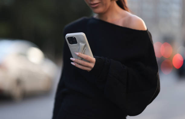 Olga Sokolenko seen wearing Say No More black off-shoulder asymmetrical oversized cotton sweater and Rhode grey silicone lip phone case, during the...