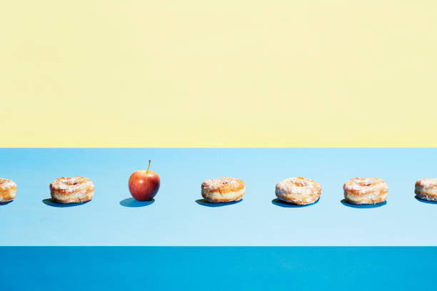 one apple in a row of donuts - junk food stock pictures, royalty-free photos & images