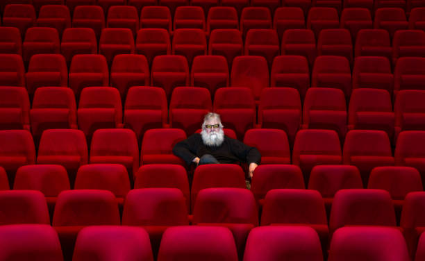 one man with white beard sits in empty cinema or theatre with comfortable red seats - concert stock pictures, royalty-free photos & images