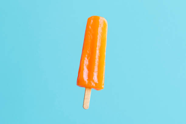 orange flavoured and colored popsicle stick on blue/turquoise background - junk food stock pictures, royalty-free photos & images