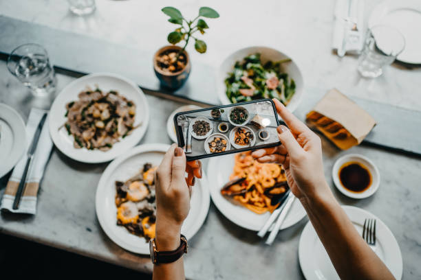 overhead view of a woman's hand taking photo of freshly served food before eating it with smartphone in a restaurant - food stock pictures, royalty-free photos & images