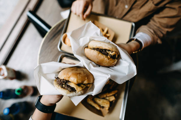 overhead view of couple sitting by the window eating burgers with french fries in a restaurant - junk food stock pictures, royalty-free photos & images