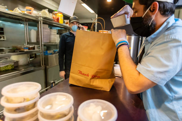 owners of local restaurant taking orders on the phone and boxing food for delivery during covid-19 pandemic - junk food stock pictures, royalty-free photos & images