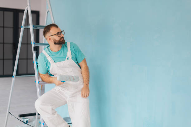 painter sits on ladder with roller by blue wall - home decoration stock pictures, royalty-free photos & images