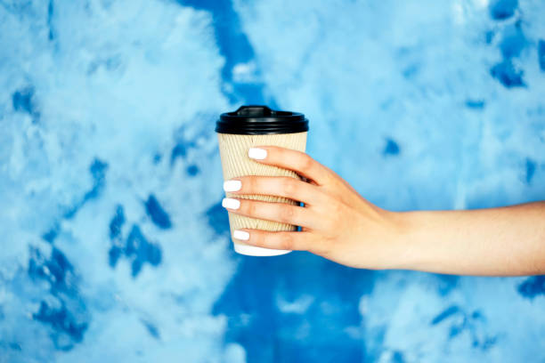 paper cup in female hands against a blue wall. - junk food stock pictures, royalty-free photos & images