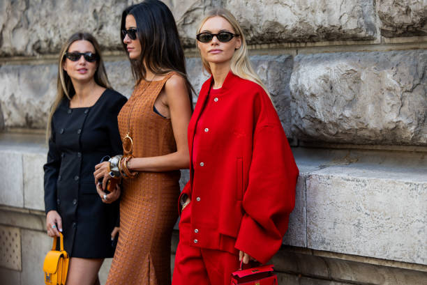 Paula Nata wears brown dress & Claire Rose Cliteur wears red oversized college jacket, bag, pants wears outside Hermes during the Womenswear...