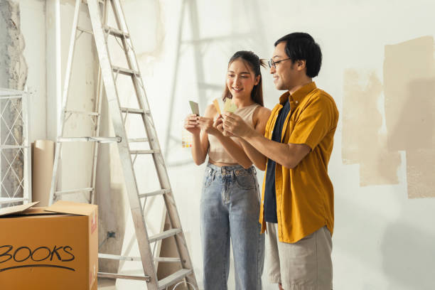 peaceful asian cheerful couple young man and woman smiling sit together on floor painting white wall with roller during renovation house relocation in new apartment happy couple painting walls - home decoration stock pictures