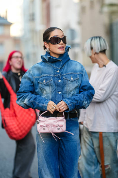 Peggy Gou wears black sunglasses, gold rings, navy blue buttoned cropped denim jean Acne Studios jacket, navy blue mid-rise washed denim jean Acne...