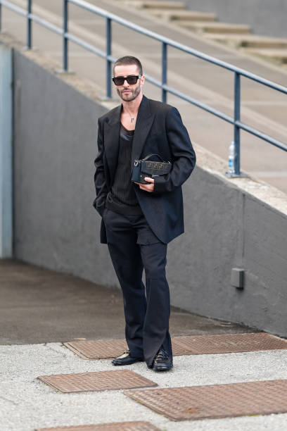 Pelayo Diaz wears black sunglasses, silver necklace, black oversized blazer jacket, black shirt, black pants, shiny black loafer moccasin leather...