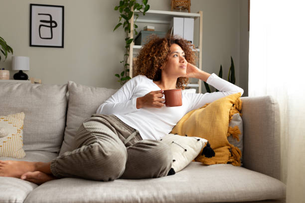 pensive multiracial woman relaxing at home, sitting on the sofa drinking morning coffee. - coffee stock pictures, royalty-free photos & images