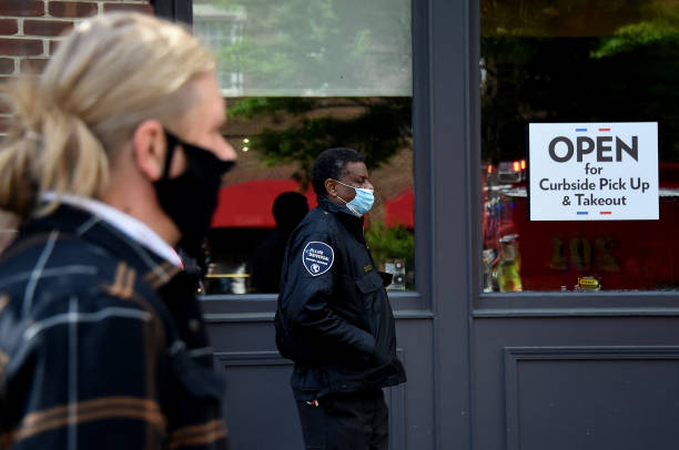 People wearing face masks wait in line in front of a restaurant open for takeout amid the coronavirus outbreak on May 11, 2020 in Alexandria,...