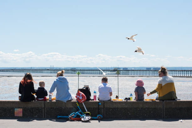 People with children sit on the seawall eating chips as various food businesses start to open for takeaway only along the promenade during the...