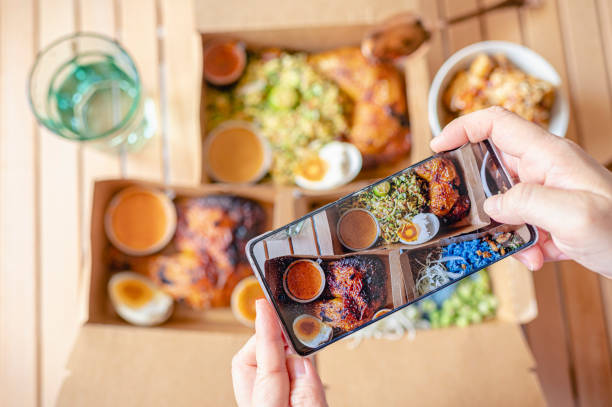 personal perspective human hand taking photo using smart phone on table top view malaysian food nasi kerabu, nasi ulam and ayam percik in recycled paper container with sauce - junk food stock pictures, royalty-free photos & i
