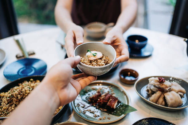 personal perspective of asian couple enjoying assorted dim sum and delicate dishes in chinese restaurant together. woman is serving a bowl of fried rice across the table to man. traditional chinese culture and food culture. y
