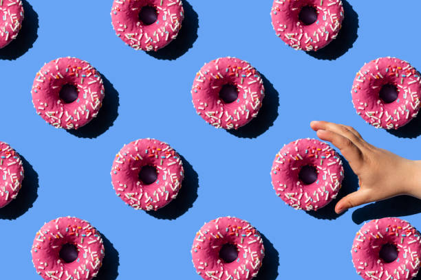 pink doughnut on pastel blue background. child's hand holding a donut. - junk food stock pictures, royalty-free photos & images