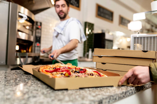 pizzaiolo at work - chef is shovelling the pizza out of the oven into the pizza box - junk food stock pictures, royalty-free photos & images