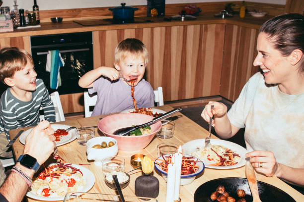 playful kids having meal with parents while sitting at dining table in home - food stock pictures, royalty-free photos & images