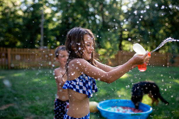 playful siblings playing with water bombs at backyard - garden decoration stock pictures, royalty-free photos & images