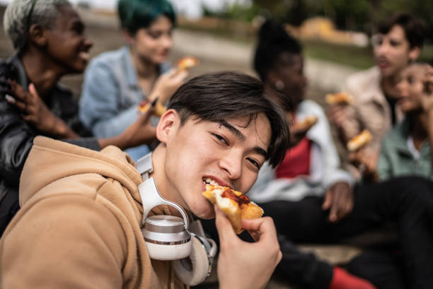 porträt eines jungen mannes, der mit freunden im park pizza isst - junk food stock-fotos und bilder