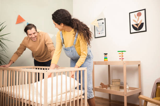 portrait of a happy couple preparing a crib for their soon to come baby - home decoration stock pictures, royalty-free photos & images