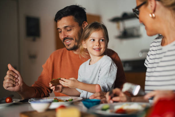portrait of a happy little girl having breakfast with her mother and father at home - food stock pictures, royalty-free photos & images