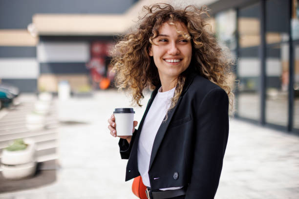 portrait of a happy, stylish young businesswoman commuting to work with a cup of coffee in her hand - junk food stock pictures, royalty-free photos & images