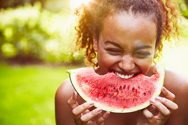 portrait of a young woman eating watermelon on a sunny day, backlit - food stock pictures, royalty-free photos & images