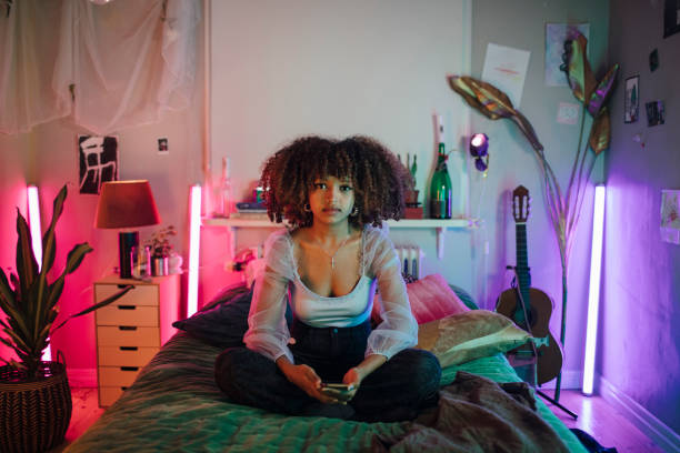 portrait of afro woman sitting with cross-legged on bed in illuminated bedroom at home - home decoration stock pictures, royalty-free photos & images
