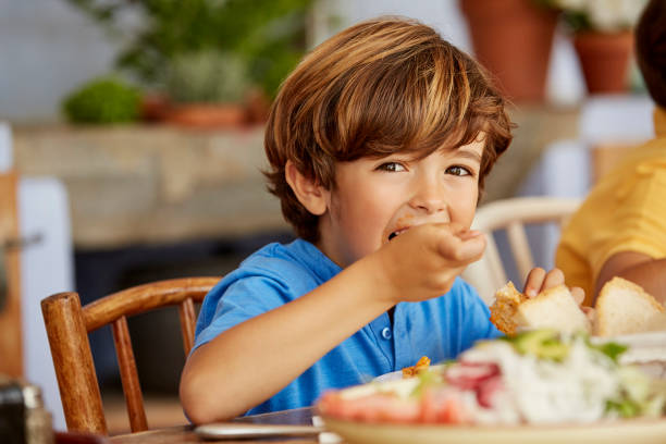 portrait of boy eating food at table in house - food stock pictures, royalty-free photos & images