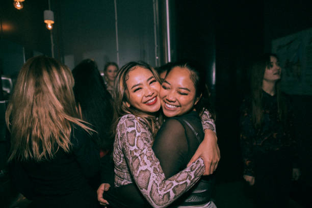 portrait of cheerful young women embracing each other while enjoying at nightclub - concert stock pictures, royalty-free photos & images