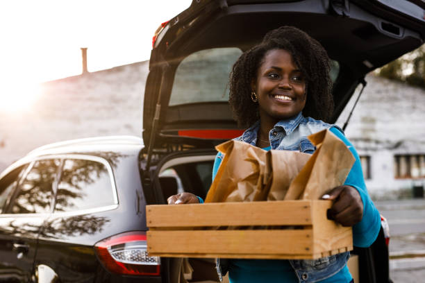 portrait of confident delivery woman holding a wooden crate with packages and order, looking away, smiling and contemplating - junk food stock pictures, royalty-free photos & images